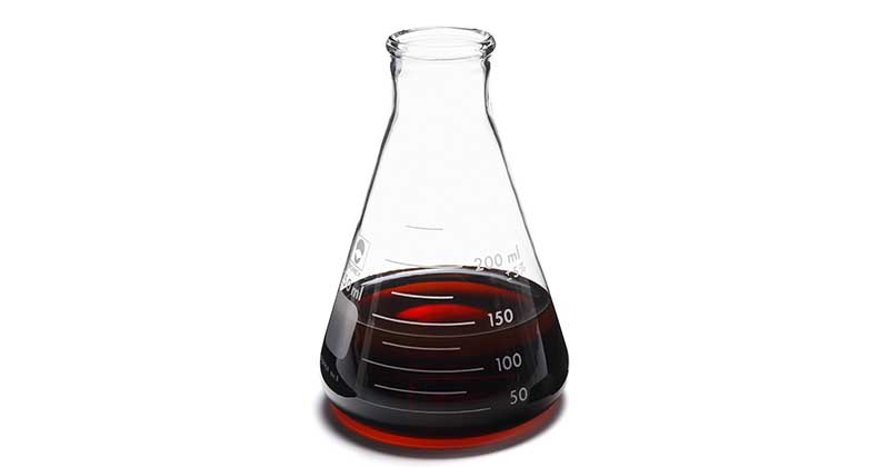 an erlenmeyer flask filled with red liquid which is a mix of resin types and catalysts called no-bake binders