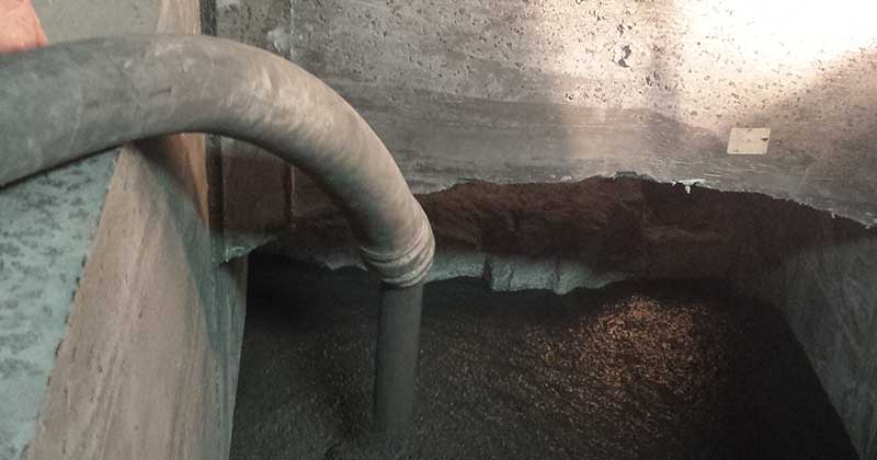 a hose pumping what looks like concrete into a concrete casing for refractory castables